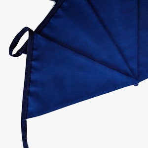 May include: A close-up of a dark blue fabric with a folded edge and a black drawstring. The fabric is folded into a triangular shape.