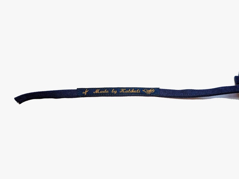 May include: A close-up of a dark blue fabric strap with a gold label that reads "Made by Kalikati".