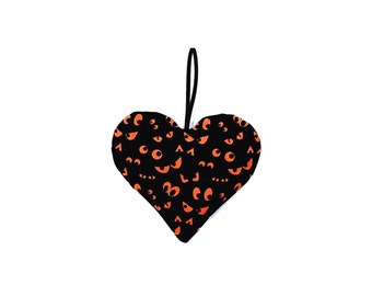 May include: A heart-shaped fabric ornament with a black background and orange eye patterns. The ornament has a black loop for hanging. The design is a Halloween theme.