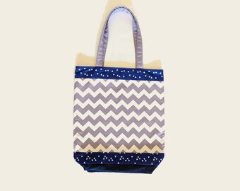 May include: A tote bag with a gray and white chevron pattern. The top and bottom of the bag are navy blue with white triangle accents. The handles are a light gray color.
