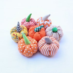 Peut inclure: Plusieurs citrouilles en tissu faites à la main, aux motifs et couleurs variés. Les citrouilles présentent des tissus orange, jaunes et blancs à pois, rayures et carreaux. Chaque citrouille a une tige verte ou beige.
