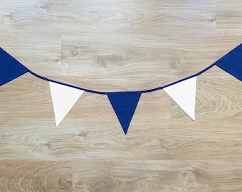 May include: A blue and white pennant banner against a wood grain background. The banner features alternating blue and white triangular flags strung together with a dark blue ribbon. The flags are evenly spaced.