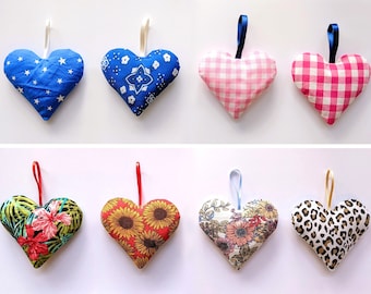 May include: Ten heart-shaped fabric ornaments with different patterns. The ornaments are made of cotton fabric and have a loop for hanging. The patterns include stars, gingham, floral, and animal print.