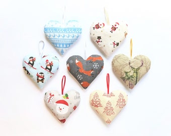 May include: Six heart-shaped fabric ornaments with different Christmas-themed patterns. The ornaments are made of a soft, textured fabric and have a loop for hanging. The patterns include penguins, foxes, reindeer, and Christmas trees.