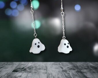 Op de afbeelding: Een paar zilveren oorhangers met witte spookbedels. De spoken hebben zwarte ogen en een kleine mond.