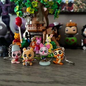 May include: A set of five Winnie the Pooh character keychains. The keychains are made of plastic and feature Piglet, Tigger, Eeyore, Pooh Bear, and a pink pig. The keychains are attached to silver chains.