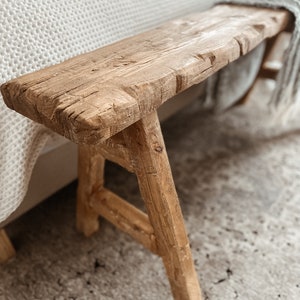 May include: A rustic wooden bench with a natural finish and a simple design. The bench has a wide, flat top and two sturdy legs. The bench is made of reclaimed wood and has a distressed look.