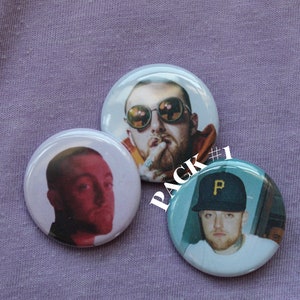 May include: Three round button pins featuring different images of the same person. The person is wearing sunglasses, a hat, and a white shirt. The text "PACK #1" is visible in the image.