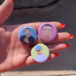 May include: Three round button pins featuring different illustrations of a man with a beard and short brown hair. The buttons are on a light blue, light purple, and light green background.