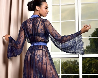 May include: A floor-length navy blue lace robe featuring long, wide sleeves and a solid satin-finish waistband. The sheer garment is crafted from intricate floral lace, showcasing a scalloped hemline and a wrap-style front with a tie closure.