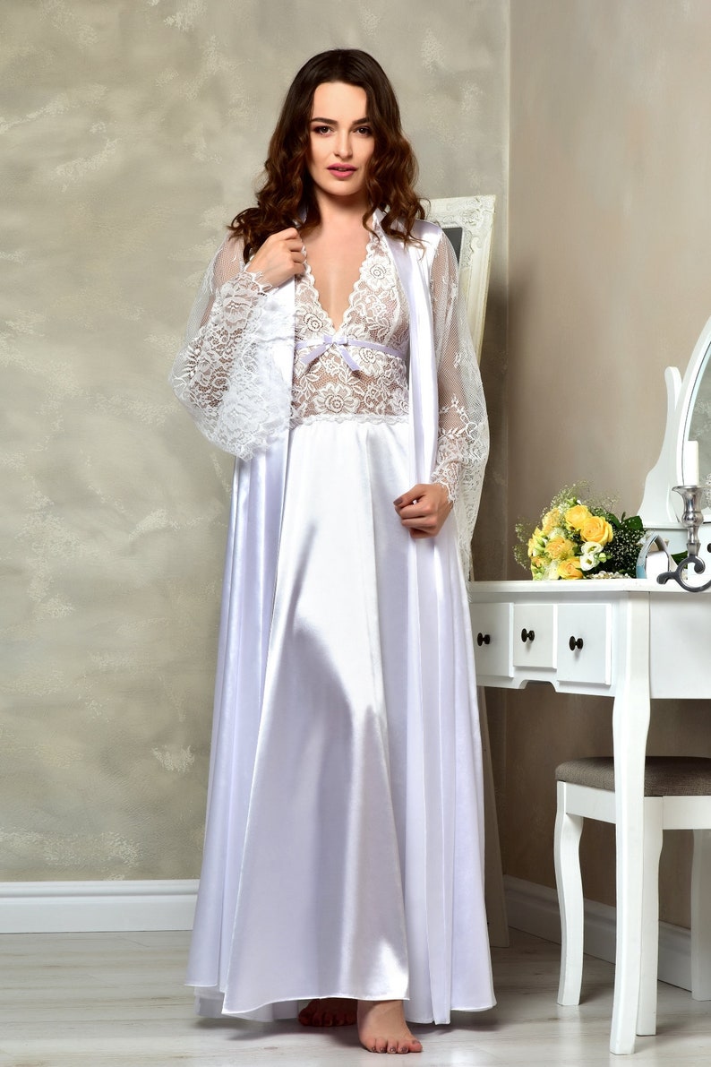 May include: A white satin nightgown with a lace overlay and a matching robe. The robe has long sleeves and a V-neckline. The nightgown has a lace bodice and a satin skirt.