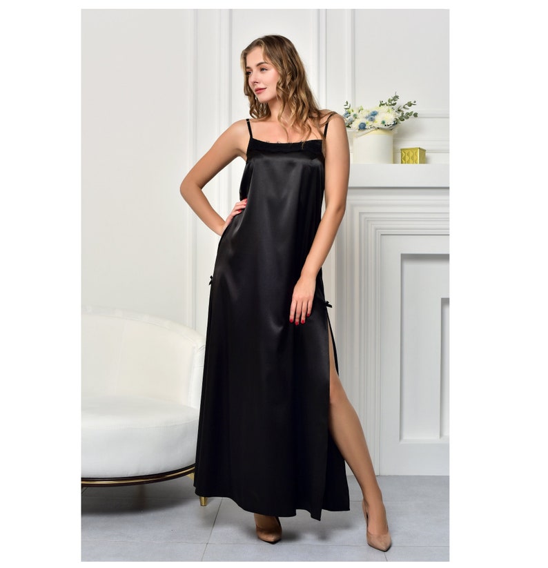 May include: A black satin slip dress with thin straps and a side slit. The dress is floor length and has a simple, elegant design.