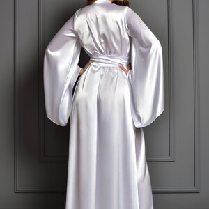 May include: A white satin robe with long sleeves and a sash tie. The robe is floor-length and has a relaxed fit.
