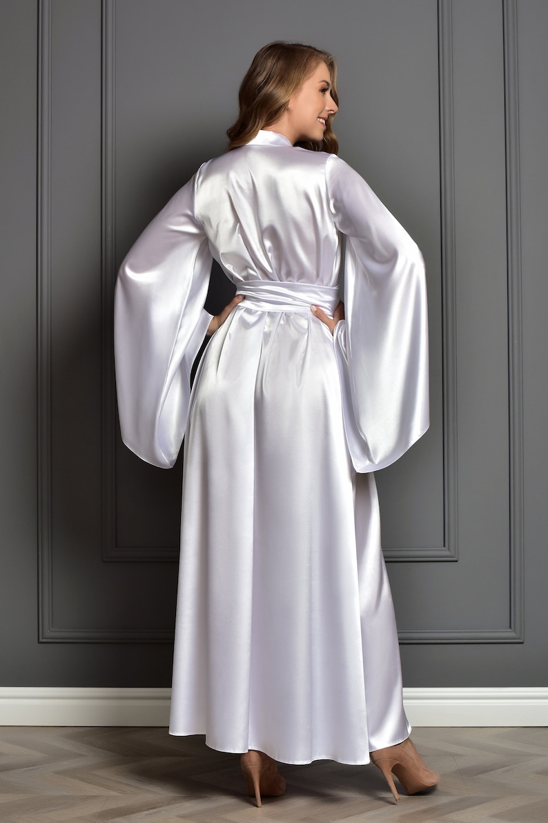 May include: A white satin robe with long sleeves and a sash tie. The robe is floor-length and has a relaxed fit.