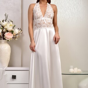 K&ouml;nnte beinhalten: Ein wei&szlig;es Satin-Nachthemd mit einem Spitzenoberteil und einem Halterneck. Das Kleid hat einen flie&szlig;enden Rock und ist perfekt zum Schlafen oder Entspannen.