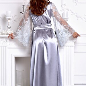 May include: A silver satin robe with long, flowing sleeves featuring delicate white lace. The robe has a sash tie at the waist and a long, flowing skirt.