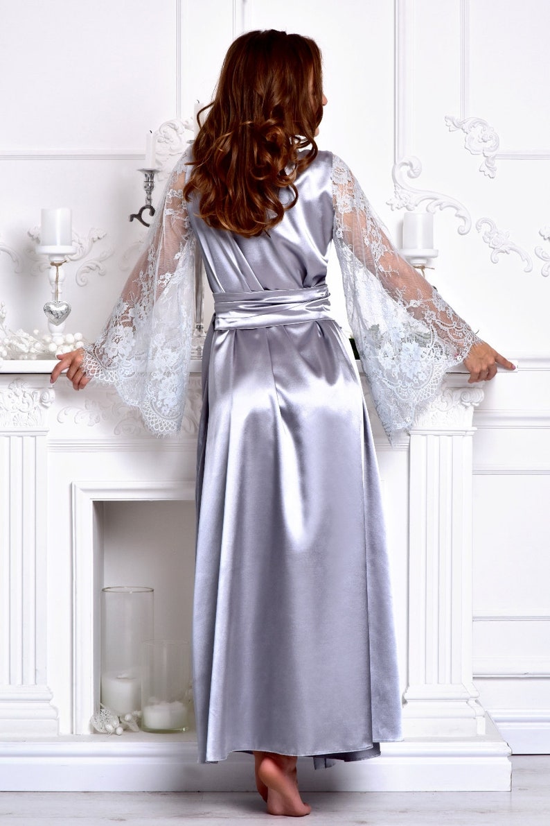 May include: A silver satin robe with long, flowing sleeves featuring delicate white lace. The robe has a sash tie at the waist and a long, flowing skirt.