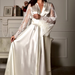 May include: A white satin robe with long, flowing sleeves featuring delicate lace detailing. The robe has a V-neckline and a sash tie at the waist.