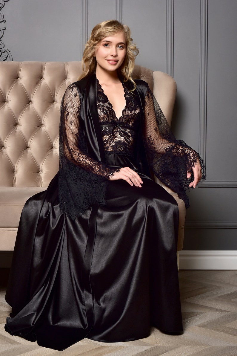 May include: A black satin robe with lace detailing and long sleeves. The robe is worn by a person sitting on a tufted couch.