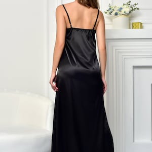 May include: A black satin slip dress with thin straps. The dress is floor length and has a simple, elegant design.