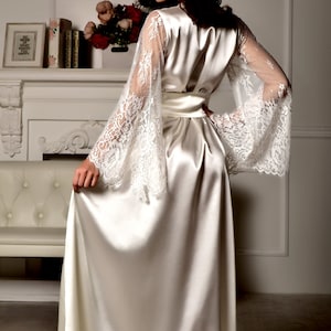 May include: A long white satin robe with lace sleeves. The robe has a sash tie at the waist.