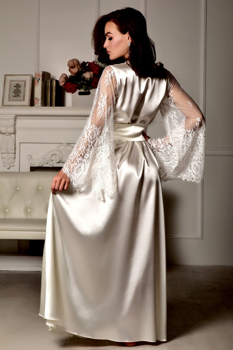 May include: A long white satin robe with lace sleeves. The robe has a sash tie at the waist.