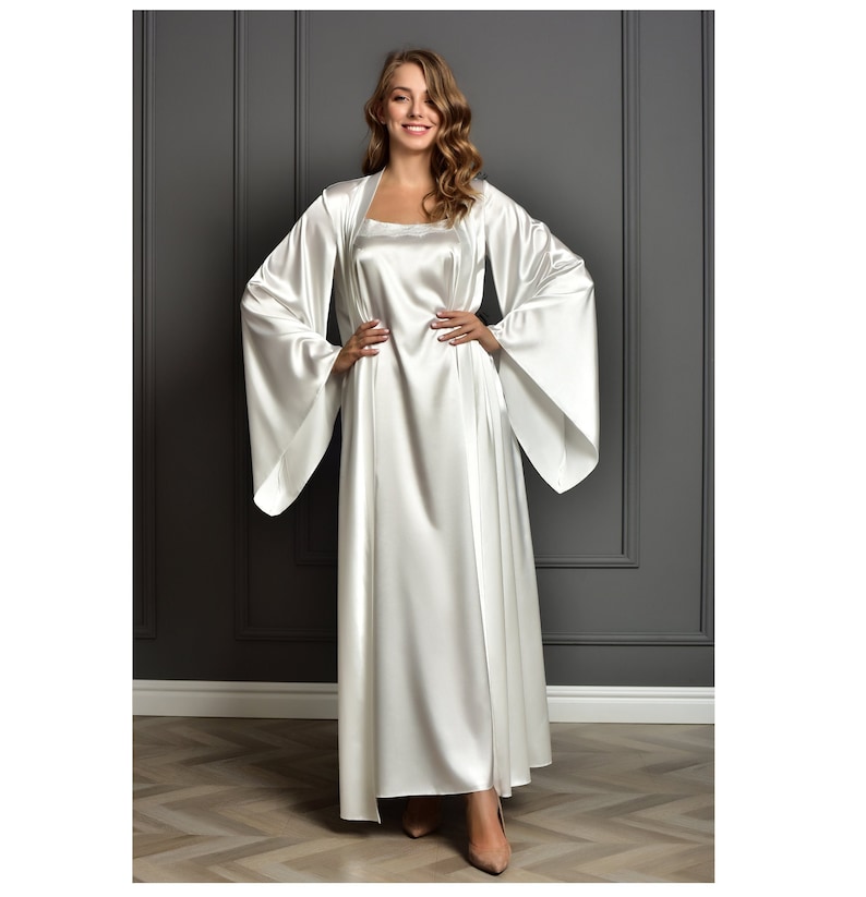 May include: A white satin robe with long sleeves and a matching slip dress. The robe has a shawl collar and a tie belt. The slip dress has a scoop neck and a straight hem.