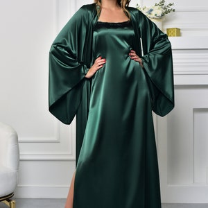 May include: A long, dark green satin robe with wide sleeves and a matching slip dress. The robe has a shawl collar and a tie closure at the waist. The slip dress has a scoop neck and a straight hemline.