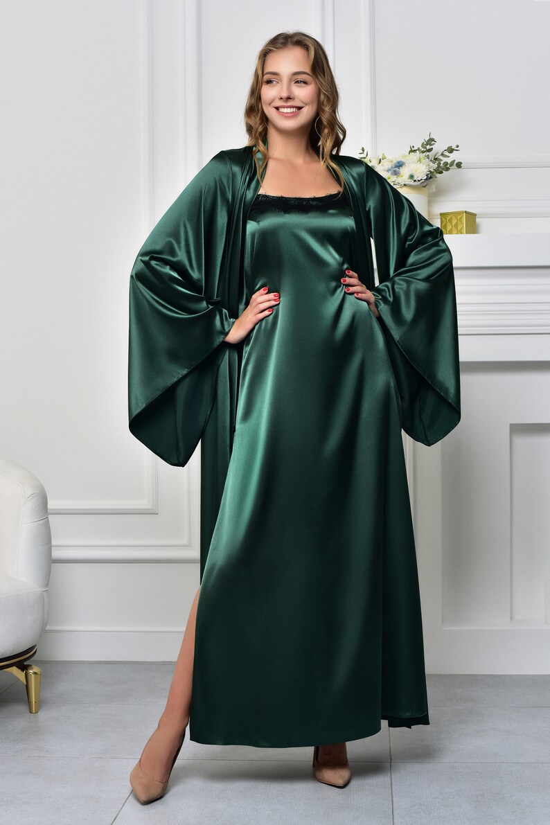 May include: A long, dark green satin robe with wide sleeves and a matching slip dress. The robe has a shawl collar and a tie closure at the waist. The slip dress has a scoop neck and a straight hemline.
