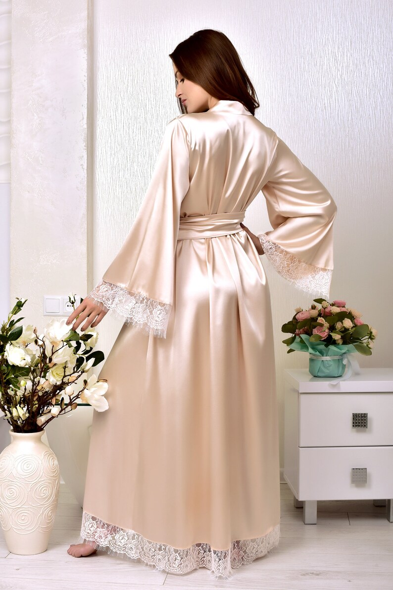 May include: A long, flowing satin robe with a lace trim. The robe is a light beige color and has a sash tie at the waist.
