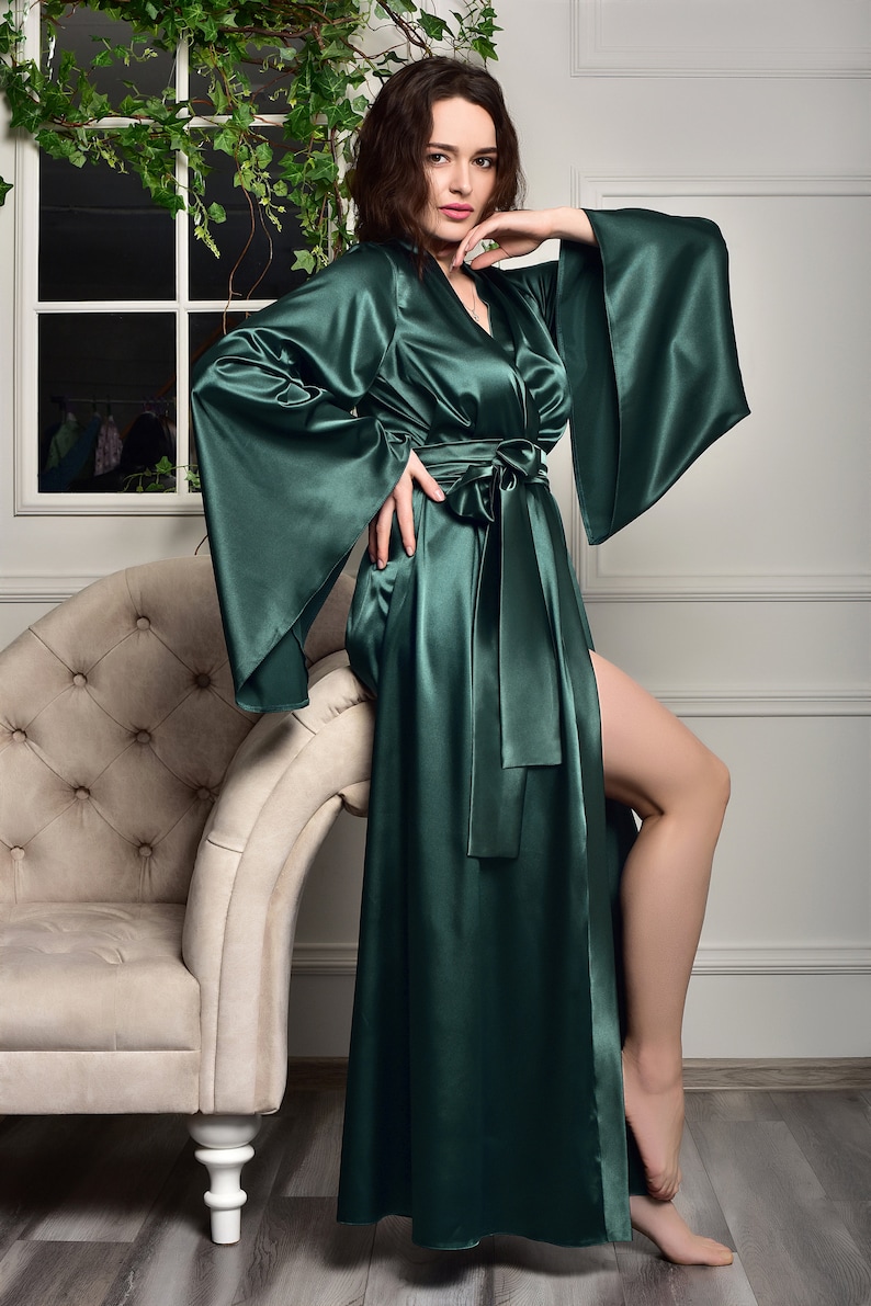 May include: A long, dark green satin robe with wide sleeves and a sash tie. The robe is open in the front, revealing a glimpse of the person's leg.
