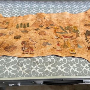 May include: A tan leather hide with colorful drawings of people, animals, and plants. The drawings are in a style reminiscent of Native American art.