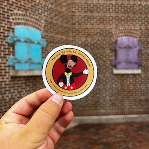 May include: A round sticker featuring a cartoon image of Mickey Mouse in a red and black suit with a yellow bow tie. The sticker reads "The one, The only, Mr. Mickey Mouse! Hello there! Welcome to my park. Now ya didn't tell!"
