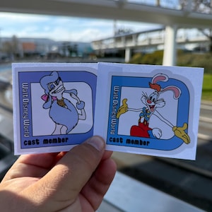 May include: Two rectangular "Cast Member" stickers featuring cartoon characters. One shows a light blue poodle with a pink bow, the other a red-haired rabbit in overalls. Both have "Walt Disney World" text.