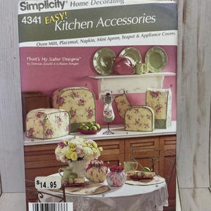 May include: A Simplicity pattern for kitchen accessories, including oven mitts, placemats, napkins, mini aprons, and appliance covers. The pattern features floral designs and the text "Kitchen Accessories".