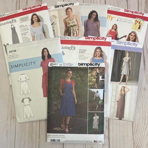 May include: A collection of Simplicity sewing pattern envelopes featuring various dress designs. The envelopes display images of the finished garments and include text such as "Amazing Fit" and "Princess Seamed Bodice."