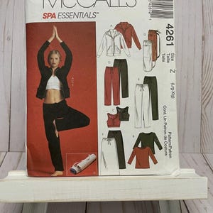 May include: A McCall's Spa Essentials sewing pattern, size Z (Lrg-Xlg). The cover features a woman in activewear, with illustrations of various outfits. The pattern includes a jacket, pants, and tops. The color scheme includes black, white, and red.