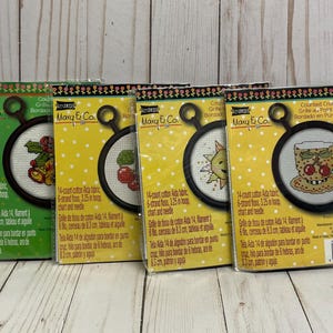 May include: Four colorful cross stitch patterns featuring a variety of designs, including a sun, cherries, a cup of coffee, and a bouquet of flowers. Each pattern is labeled with the brand "Mary & Co." and includes details about the fabric, floss, hoop size, and chart.