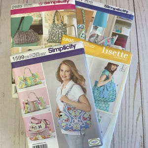May include: Several Simplicity sewing patterns for handbags are displayed, featuring colorful designs and illustrations. The patterns include various styles, with the numbers 2685, 1599, 1905, and 2617 visible. The patterns showcase different bag shapes and fabric patterns.