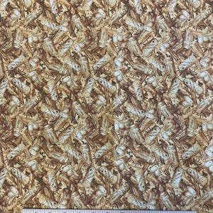 May include: Fabric with a repeating pattern of wine corks and bottles in shades of brown and beige. The corks are labeled "Merlot". A ruler is at the bottom of the image.