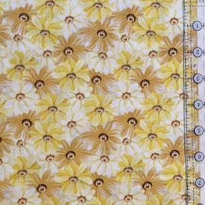 May include: Close-up of a fabric with a repeating floral pattern. The design features daisies in shades of yellow and brown against a cream background. A ruler is visible on the right side of the image, showing measurements in inches.