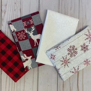 May include: Four fabric squares with a winter theme. The squares feature a red and black buffalo plaid, a gray and red plaid with a white deer, a white fabric with a subtle texture, and a gray fabric with a white woodgrain pattern and red snowflakes.