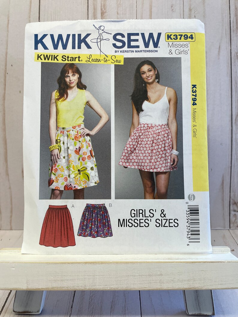 May include: A sewing pattern for a skirt in girls' and misses' sizes. The pattern is from Kwik Sew and is called "Learn-to-Sew". The pattern shows three different skirts, one with a floral print, one with a red and white print, and one with a purple and white print.