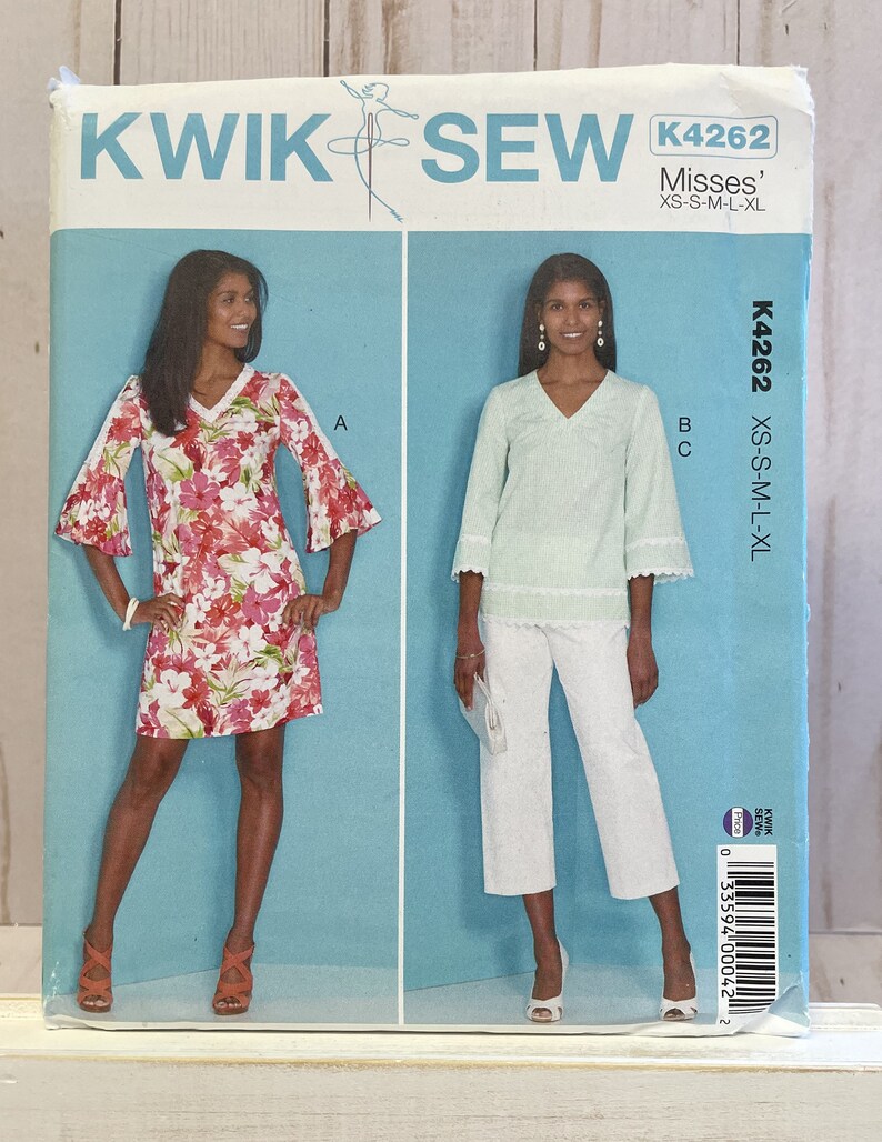May include: Sewing pattern envelope for a women's top and pants. The pattern is called Kwik Sew K4262 and is for sizes XS-S-M-L-XL. The envelope shows two models wearing the garments. The model on the left is wearing a floral print top with 3/4 sleeves. The model on the right is wearing a light blue top with 3/4 sleeves and white pants.