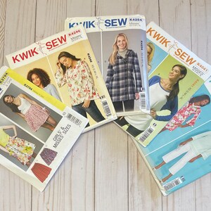 May include: Five different sewing patterns for women's clothing. The patterns are from the brand Kwik Sew and feature different styles, including a blouse, a skirt, a jacket, and pants. The patterns are printed on white paper with colorful illustrations and text.