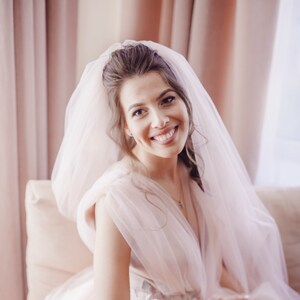 May include: A bride in a pink tulle wedding dress with a veil and a small chihuahua dog sitting on her lap.