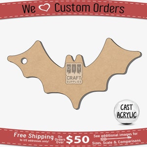 Può includere: Una sagoma di pipistrello in legno marrone con un foro nella parte superiore. Il pipistrello è su uno sfondo bianco. Il testo "DIY CRAFT SUPPLIES" è in una casella bianca sul pipistrello. Il testo "CAST ACRYLIC" è in un cerchio bianco con bordo nero.