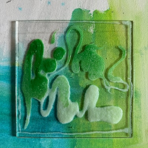 May include: A square glass coaster with a green and white abstract design. The design is raised and textured, giving the coaster a 3D effect.