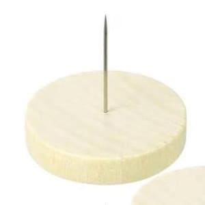 Może przedstawiać: Okrągły, kremowy przedmiot przypominający ser, z srebrnym metalowym szpikulcem pośrodku. Obiekt ma teksturowaną powierzchnię i cylindryczny kształt. Tło jest jednolicie białe.