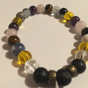 May include: A beaded bracelet featuring a range of colourful stones, including amethyst, rose quartz, tiger's eye, aquamarine, and clear quartz. The bracelet also includes a black lava rock bead with a gold accent.